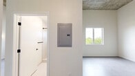 Located at 315 NW 32nd Street in Miami's vibrant Wynwood neighborhood, this one-bedroom, one-bathroom unit offers a thoughtfully designed layout with modern finishes throughout. The space is defined by its impressively tall ceilings, which lend an open, airy quality that belies its compact footprint. Large-format gray tile flooring runs seamlessly through the main living areas and bedroom, providing a clean, contemporary aesthetic.

The spacious bedroom benefits from abundant natural light through a generous window overlooking a lush tree canopy, offering a serene outdoor view. Modern oval wall sconces accent the crisp white walls, adding a stylish architectural touch. The bedroom also features a well-organized built-in closet system with open shelving, hanging rails, and a built-in desk surface — maximizing storage and functionality.

An in-unit stacked washer and dryer is conveniently tucked into a dedicated nook adjacent to the bedroom, offering practical everyday convenience. The kitchen is visible beyond, fitted with sleek dark cabinetry and a contrasting countertop with a modern sink.

The bathroom is finished with large-format white tile, an open walk-in shower with matte black fixtures, a wall-mounted toilet, and a navy vanity with a light countertop. A small frosted window provides natural ventilation. The overall ambiance is clean, minimalist, and modern — ideal for urban living in Miami.