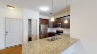 Located at 1109 Matteo Dr in Wilmington, NC, this single-floor residence offers a well-designed layout with a blend of functional and stylish finishes throughout. The open-concept living and kitchen area is anchored by warm hardwood flooring that extends from the entry through the main living space. The kitchen is a standout feature, showcasing rich dark-toned cabinetry, granite countertops, a double-basin stainless steel sink set into a peninsula, pendant lighting, and a full suite of stainless steel appliances including a refrigerator, electric range, and built-in microwave. A pantry closet provides additional storage conveniently adjacent to the kitchen. The bedrooms are carpeted and fitted with ceiling fans for year-round comfort, with natural light entering through slatted blinds. One bedroom offers direct access to a private balcony, adding outdoor living space. The bathrooms are finished consistently with granite-topped dark wood vanities and tile flooring, each equipped with a tub-shower combination. Walk-in closets with wire shelving provide ample storage. The overall aesthetic is clean, neutral, and move-in ready, reflecting a cohesive and practical design suited for comfortable everyday living.