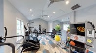 Located at 1500 Sunbow Ln in Raleigh, NC, this single-story fitness facility is designed to support a full range of workout activities in a bright, functional environment. The space features vaulted ceilings that lend an open, airy feel, complemented by dual ceiling fans and recessed lighting that ensure proper airflow and visibility throughout. Natural light filters in through windows on multiple walls, enhancing the welcoming atmosphere.

The geometric, multi-toned flooring in shades of blue, gray, and natural wood tones adds a dynamic visual element while providing a durable surface suited for varied exercise activities. A large wall mirror expands the perceived space and allows for form-checking during workouts.

The facility is outfitted with a range of cardio machines, including a True elliptical and treadmill, alongside a multi-function strength training station and a dumbbell rack. Fitness accessories such as stability balls, medicine balls, and an AbSolo core trainer round out the equipment offerings. The overall ambiance is clean, modern, and energizing, making it a practical and motivating environment for fitness-focused use.