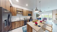 This thoughtfully designed single-floor residence offers a seamless open-concept layout that connects the kitchen, dining, and living areas into one cohesive and functional space. The kitchen is a standout feature, showcasing warm wood-grain cabinetry that extends floor to ceiling, a white subway tile backsplash, light quartz countertops, and a suite of stainless steel appliances including a French door refrigerator, dishwasher, and range. A large peninsula with pendant lighting above serves as both a prep area and a casual dining bar. The living room is bright and inviting, benefiting from large sliding glass doors that open to a private balcony with lush outdoor views. Light tile flooring runs throughout, adding a clean, contemporary feel. The bedroom is a comfortable retreat with a window framing greenery views, a closet, and direct access to the bathroom. The bathroom features warm wood vanity cabinetry, a light quartz countertop, an illuminated mirror, and a separate closet space housing a stacked in-unit washer and dryer. Recessed lighting and ceiling fans throughout contribute to the overall bright and airy ambiance of the home.