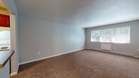 Located in the Northridge neighborhood of Wallingford, Connecticut, this single-floor residence offers a practical and well-organized layout. The spacious living room is finished with wall-to-wall carpet, neutral gray walls, and a large window that invites natural light and views of the surrounding greenery. Baseboard heating is present throughout the carpeted areas, ensuring year-round comfort. The kitchen is open to the living space via a pass-through cutout, creating a connected, functional flow. It features warm-toned wood cabinetry, dark countertops, light hardwood-style flooring, and white appliances including a refrigerator and electric range with overhead ventilation. The bedroom is generously sized with plush carpeting, a ceiling fan with light fixture, and a window overlooking lush outdoor foliage. Ample storage is provided through a standard closet and an additional walk-in closet with built-in shelving. The bathroom is clean and well-appointed, with light wood-style flooring, a full tub and shower enclosure with white tile surround, and a vanity with dark cabinetry. Throughout the residence, a consistent neutral color palette and clean finishes create a calm, livable atmosphere.