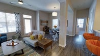 This contemporary single-floor residence showcases a thoughtfully designed open-concept layout that seamlessly connects the living and dining areas. Rich, dark hardwood flooring runs throughout, providing a warm and sophisticated foundation that contrasts elegantly with the neutral-toned walls. Structural columns with subtle brick detailing add a touch of architectural character to the space.

The living area is bright and welcoming, benefiting from large windows that usher in generous amounts of natural light. A modern pendant light fixture anchors the dining area, which comfortably accommodates a round table and seating — ideal for both casual meals and entertaining. The space between the two areas flows effortlessly, creating a sense of openness and ease of movement.

Neutral wall tones throughout the home serve as a versatile backdrop, complementing a range of furnishing styles. The overall ambiance is clean, modern, and inviting, with a balanced interplay of light and texture. Ceiling fans and recessed lighting add to the functional design while maintaining a polished aesthetic. The layout maximizes livability while keeping the overall feel airy and uncluttered — a well-appointed space suited for comfortable everyday living.