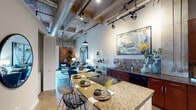 This two-bedroom, two-bathroom residence in Houston's 77021 corridor showcases an industrial-chic aesthetic rooted in authentic architectural character. The open-concept living and kitchen area is defined by soaring ceilings with exposed concrete beams, visible ductwork, and track lighting that collectively evoke a converted warehouse aesthetic. Original brick accent walls add warmth and texture, grounding the space with a sense of history.

The kitchen is well-appointed with rich wood cabinetry, granite countertops, tile backsplash, black appliances including a refrigerator and range, and a large island that doubles as a casual dining surface. The living area flows naturally from the kitchen, providing ample room for seating and entertaining beneath a ceiling fan that anchors the space.

Both bedrooms offer generous proportions, with the primary bedroom benefiting from wide windows that draw in natural light and provide open views of the surrounding area. Exposed brick and concrete columns continue the industrial theme throughout.

Each bathroom features granite vanity countertops, wood cabinetry, and a shower-tub combination. Polished concrete and stone-look flooring run throughout, tying all rooms together cohesively and reinforcing the unit's distinctive urban character.