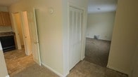 This two-floor space is designed with a straightforward, functional layout that emphasizes practicality and ease of living. The interior showcases neutral beige walls throughout, creating a calm and cohesive atmosphere that works well as a versatile backdrop for a variety of furnishing styles.

The flooring transitions between carpet and hard surface tile, providing comfort in living and resting areas while offering durability in transitional zones. White baseboards and trim work run consistently throughout, lending a clean, polished finish to each room.

A notable feature is the louvered bi-fold closet door, which offers convenient storage access while contributing a classic architectural detail to the hallway area. A panel door with brass hardware is also visible, maintaining the traditional aesthetic of the space.

The open sight lines between rooms suggest a connected, flowing floor plan that allows natural movement between spaces. The carpeted area visible beyond the hallway provides a comfortable, quiet area suitable for use as a living or sleeping space. Overall, the space maintains a tidy, neutral character well-suited for everyday living across both floors.