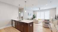 This well-designed two-bedroom, two-bathroom unit offers a thoughtfully arranged single-floor layout that maximizes its footprint through an open-concept living and kitchen area. Light wood-tone flooring runs throughout the unit, lending warmth and visual continuity across all rooms.

The kitchen serves as a central feature, anchored by a large island with a white quartz countertop, an undermount sink, and seating for bar stools. Rich dark-wood cabinetry extends to the upper walls, complemented by stainless steel appliances including a French door refrigerator, electric range, and microwave. Pendant lights hang above the island, adding an elevated design touch.

The open living and dining area benefits from large windows fitted with roller shades, allowing ample natural light while maintaining privacy. A ceiling fan with integrated lighting adds both function and comfort to the space.

Both bedrooms are comfortably scaled, featuring large windows, ceiling fans, and dedicated closets. The primary bedroom offers a quiet, neutral retreat. The two bathrooms are finished consistently, each featuring dark wood vanities, quartz countertops, and light tile flooring — one with a soaking tub and the other with a glass-enclosed walk-in shower.