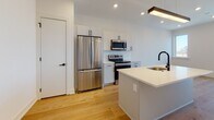 Located in the vibrant South Philadelphia neighborhood of 19147, this single-floor space at 1331 S Juniper Street offers a clean, contemporary design with thoughtful finishes throughout. The open-concept layout seamlessly connects the kitchen and living area, creating a bright and airy atmosphere enhanced by recessed lighting and warm natural light.

The kitchen is a standout feature, showcasing white shaker-style cabinetry, subway tile backsplash, and a full suite of stainless steel appliances including a French door refrigerator, electric range, and over-the-range microwave. A central island with a white quartz countertop and a matte black faucet provides additional workspace and serves as a natural gathering point. A modern pendant light fixture adds an elegant touch above the island.

Wide-plank light oak hardwood flooring flows continuously through the open living and kitchen spaces, contributing to the warm, cohesive feel of the interior. A separate bedroom area features two large windows that flood the room with natural light and offer views of the surrounding Philadelphia cityscape.

The bathroom is finished with neutral large-format tile flooring, a floating vanity with black hardware, and a frameless mirror, maintaining the modern aesthetic found throughout the space. Clean white walls and crisp trim complete the fresh, move-in-ready presentation of this well-designed Philadelphia residence.