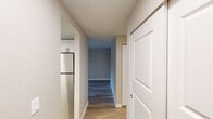 This single-floor residence offers a clean, modern aesthetic with a thoughtfully designed layout. The kitchen is a functional highlight, featuring crisp white shaker-style cabinetry, light countertops, a stainless steel sink, and stainless steel appliances including a refrigerator and dishwasher. A skylight overhead brightens the space, while light hardwood-style flooring adds warmth and continuity throughout the kitchen and hallway areas.

The living room is a comfortable and inviting space, anchored by a tile-surround fireplace that serves as a natural focal point. Built-in shelving on an adjacent wall provides practical storage and display space, while the same hardwood-style flooring ties the room together with a cohesive, contemporary feel.

The bedrooms are finished with soft, neutral-toned carpet and feature baseboard heating units for comfort. Each room is served by a window with blinds that allow natural light to filter in while offering privacy, with views of lush greenery outside.

A central hallway connects the key areas of the unit, with a sliding closet door offering additional storage. The neutral color palette used throughout — warm beige walls, white trim, and light flooring — creates a calm, airy ambiance that makes the space feel open and move-in ready.