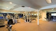 This single-level fitness space is designed to accommodate a comprehensive range of workout activities. The room is generously proportioned, providing ample floor space for both strength training and cardiovascular exercise. A textured ceiling with recessed lighting and a skylight panel ensures the area is well-illuminated throughout. Structural support columns are integrated into the layout, and the carpeted flooring adds comfort underfoot during workouts.

The strength training section features a multi-station cable machine along with a weight bench and free weights, offering a variety of resistance training options. The cardio section is lined with multiple treadmills and additional aerobic machines, arranged to maximize the usable floor area. Full-length mirrors span multiple walls, visually expanding the space while allowing users to monitor their form. A wall-mounted air conditioning unit supports climate control within the room.

Overall, the space presents a practical and organized fitness environment, combining essential equipment with thoughtful layout design to support a well-rounded exercise routine.