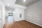 This contemporary single-floor unit showcases an industrial-modern aesthetic defined by a striking combination of exposed concrete ceilings and accent walls, warm hardwood flooring, and crisp white walls throughout. The open-concept living and dining area is bathed in natural light from expansive floor-to-ceiling windows, offering broad urban views and creating an airy, spacious atmosphere. Recessed lighting complements the natural illumination throughout the unit.

The kitchen is thoughtfully designed with flat-front wood-grain cabinetry, stainless steel appliances including a range, built-in microwave, dishwasher, and refrigerator, as well as a sleek composite countertop and a subway tile backsplash. A kitchen island provides additional workspace and casual dining potential.

The bathroom features large-format tile flooring, a combined soaking tub and shower enclosed by a sliding glass door, a wood-grain vanity with dark countertop and undermount sink, and clean, modern fixtures throughout.

A generously sized walk-in closet includes extensive built-in shelving and hanging systems, offering excellent organizational capacity. An electrical panel is also conveniently integrated into the entryway. The overall design balances raw, industrial elements with refined modern finishes, resulting in a cohesive and functional living space.