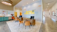 Located at 1005 Brentwood Dr in Davenport, Florida, this single-story community clubhouse offers a generously proportioned, thoughtfully designed interior with a bold coastal-contemporary aesthetic. The welcoming entrance sets the tone immediately, featuring dual curved wooden reception desks, warm amber seating, and a striking watercolor mural backdrop lit by a yellow neon sign reading "Meet Me On The Bright Side." Slatted wood ceiling accents and polished concrete floors flow throughout, lending the space a bright, upscale character.

The open-plan living, dining, and kitchen area is anchored by exposed wood beams, statement chandeliers, and plush seating arrangements bathed in natural light from large windows. Adjacent to this is a spacious game room with a dramatic grid-pattern ceiling light installation, shiplap accent walls, and a wall-mounted display screen. Three private office spaces offer individual workstations with terrazzo-style flooring, whiteboard panels, and warm wall sconces — two finished in a vibrant golden-orange palette with glass sliding doors. Two den areas and a bonus room provide additional flexible gathering spaces. The combination of polished concrete floors, curated artwork, layered lighting, and a cohesive warm color palette creates a lively yet functional environment throughout.