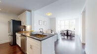 Located at 65 Bay St in Jersey City, NJ, this well-designed single-floor residence offers a clean, contemporary aesthetic throughout. The open-concept layout seamlessly connects the kitchen, living, and dining areas, all anchored by rich, dark hardwood flooring that extends across the main living spaces.

The kitchen is a functional centerpiece, featuring white shaker cabinetry, dark stone countertops, stainless steel appliances including a range, over-the-range microwave, and refrigerator, as well as a peninsula with an undermount sink that opens directly to the living and dining areas. Large windows in the living and dining zones allow abundant natural light to fill the space, creating a bright and airy atmosphere.

The living area provides a comfortable and understated setting, highlighted by a neutral color palette, crisp white walls, and framed botanical artwork. The bedroom is a serene retreat with a generous window offering expansive views of the Jersey City skyline and surrounding landscape, complemented by the same warm hardwood flooring.

The bathroom is finished with large-format tile flooring, a marble-topped vanity with white cabinetry, a mirrored medicine cabinet, and a glass-enclosed walk-in shower with tile surround, delivering a polished and functional space.