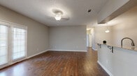 Located at 1290 W Government St in Brandon, Mississippi, this single-story, 3-bedroom, 2-bathroom home offers a functional and comfortable layout. The expansive living room is a standout feature, showcasing rich, dark hardwood-style flooring, neutral gray walls, a textured ceiling, and a ceiling fan with light fixture that ties the space together. The open layout connects seamlessly to the kitchen via a raised breakfast bar with decorative wrought-iron corbels and a pendant light overhead, making it ideal for everyday living and entertaining. The galley-style kitchen is well-appointed with dark wood cabinetry, granite-look countertops, stainless steel appliances including a refrigerator and dishwasher, and matching hardwood-style flooring. The three bedrooms offer a quieter retreat, with plush carpeting, neutral tones, and closet space. The primary bedroom is generously sized and includes its own closet. Both bathrooms are practical and clean, featuring tub-shower combinations with curtain rods and hardwood-style flooring. A dedicated laundry room adds convenience. Throughout the home, consistent neutral paint, white trim, and cohesive flooring choices create a clean, move-in-ready atmosphere.