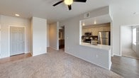 This single-floor residence offers a well-appointed, open layout that seamlessly connects the living and kitchen areas. The living room features neutral-toned carpeting, a ceiling fan with light fixture, and French doors that invite natural light while providing access to an outdoor space. The open-concept kitchen is equipped with stainless steel appliances, including a range, over-the-range microwave, and refrigerator, complemented by light-toned cabinetry, a dark tile backsplash, and stone-finish countertops. A peninsula countertop with a built-in sink extends into the living area, making it ideal for casual dining or entertaining. The bedroom is generously proportioned with plush carpeting, a ceiling fan, and its own set of French doors offering additional outdoor access and natural light. The bathroom features a long vanity with dual vessel sinks, gray cabinetry, light stone countertops, and large mirrors, all set atop rich dark hardwood-style flooring. Recessed lighting adds warmth throughout. The overall aesthetic is clean and contemporary, with a neutral color palette and modern finishes that create a bright, cohesive living environment.