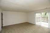 This single-floor residence offers a practical and comfortable layout across several well-defined living areas. The main living space is generously sized, featuring neutral-toned wall-to-wall carpeting and crisp white walls that create a clean, open atmosphere. A large sliding glass door with vertical blinds floods the area with natural light and provides access to the outdoors. The living space flows seamlessly into a secondary area equipped with a ceiling fan, offering additional room for dining or lounging, with a glimpse of the kitchen just beyond.

The kitchen is outfitted with rich, dark wood cabinetry that provides ample storage above and below the counters. Light-colored countertops offer generous prep space, and the kitchen includes a gas range, dishwasher, and full-size refrigerator. The tile flooring adds a durable, easy-to-clean surface suited for a busy kitchen environment.

The bathroom features an extended granite-style countertop with a single sink, framed by a large mirror and wall-mounted lighting fixtures. A separate shower area and closet add further functionality to this well-organized space.

The bedroom is a quiet, carpeted retreat with neutral walls and multiple electrical outlets, offering a blank canvas for personalization. Overall, the space delivers a straightforward and livable design.