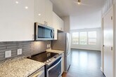 Located at 455 S Maple Ave in Falls Church, Virginia, this well-appointed one-bedroom, one-bathroom residence offers a thoughtfully designed layout across a single floor. The kitchen is outfitted with stainless steel appliances including a electric range, over-the-range microwave, French door refrigerator, and dishwasher. Granite countertops, a subway tile backsplash, and crisp white upper cabinetry with modern hardware complement the warm wood-tone lower cabinetry, creating a clean, contemporary aesthetic. Hardwood-style flooring extends through the kitchen and into the open-concept dining and living area, which benefits from a large window that fills the space with natural light and offers views of the surrounding neighborhood. A stacked washer and dryer is conveniently integrated near the kitchen, adding in-unit laundry functionality. The bedroom features soft carpeting, bright white walls, and two windows that invite ample daylight and outdoor views. Two closets provide generous storage throughout the unit. The bathroom is finished with large-format white tile flooring, a tub-shower combination with grey subway tile surround, dark espresso cabinetry, and granite countertops, delivering a refined and cohesive look throughout the home.
