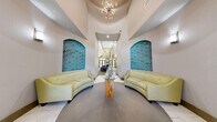 The Clubhouse and Business Center at 5300 Outlook Blvd in Pueblo, Colorado is a thoughtfully designed community facility that seamlessly blends comfort, style, and functionality across a single floor. The space makes an immediate impression with a dramatic rounded entryway foyer, featuring soaring ceilings, a contemporary sputnik chandelier, and a pair of teal tufted arched wall niches flanking curved cream leather sofas arranged around a natural wood pedestal coffee table — an inviting and visually striking reception area.

Beyond the foyer, the open living area offers a comfortable lounge with a plush sectional sofa, accent chairs, and a fireplace crowned by a teal feature wall with a mounted flat-screen TV. Vibrant artwork and large windows along one wall fill the room with natural light, while high-top bistro tables with lime green chairs provide flexible seating for casual gatherings or work sessions.

The fully equipped kitchen is both practical and stylish, showcasing rich dark cabinetry, granite countertops, a mosaic tile backsplash, stainless steel appliances including a gas range and refrigerator, and pendant lighting over a breakfast bar with counter seating. The cohesive aqua-toned accent walls throughout tie the entire space together, creating a lively yet professional atmosphere suited for community events and everyday use.
