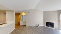 This single-story residence is designed with a clean, neutral palette and functional layout throughout. The main living area is a standout, featuring vaulted ceilings that enhance the sense of openness, light wood-look laminate flooring, and a tile-surround fireplace that serves as a focal point. A sliding glass door allows natural light to filter in and provides outdoor access. The kitchen is thoughtfully designed with white cabinetry, white countertops, a stainless steel sink with a brushed gold faucet, a dishwasher, and a refrigerator, complemented by light laminate flooring and overhead lighting.

The bedrooms are carpeted for comfort and each include a ceiling fan with light fixture and windows that bring in natural light. One bedroom connects to a primary bathroom featuring a wide vanity with white cabinetry, a large mirror, and a tub-shower combination. A walk-in closet with multi-tiered shelving and hanging rods offers generous storage. A second full bathroom mirrors similar finishes, including a single-sink vanity and a tub-shower combo. Consistent neutral tones and laminate flooring tie the common areas together cohesively.
