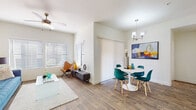 This well-designed single-floor residence offers a cohesive modern aesthetic defined by warm wood-look flooring, neutral walls, and abundant natural light throughout. The open-concept living area features a ceiling fan, large windows with horizontal blinds, and generous space for both lounging and entertaining. It flows naturally into a defined dining area, complete with a pendant chandelier and access to a sliding glass door leading outdoors. The kitchen is thoughtfully outfitted with two-tone cabinetry — white upper and gray lower — paired with white quartz countertops, stainless steel appliances including a range, microwave, and sink, plus a tile backsplash and a high window for added light. The residence includes multiple bedrooms, each bathed in natural light from sizable windows. The primary bedroom benefits from a ceiling fan and direct access to a bathroom featuring a gray vanity, tub-shower combo, and a walk-in closet with built-in shelving. A second full bathroom mirrors the clean, contemporary finish with a gray vanity and tub-shower combination. Throughout, the design emphasizes clean lines, functional layouts, and a bright, inviting ambiance.