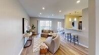 Located at 3130 Normandy Woods Dr in Ellicott City, Maryland, this well-appointed single-floor residence offers a thoughtfully designed layout that balances comfort and modern style. The open-concept living and dining area is anchored by warm hardwood-style flooring, recessed lighting, and large sliding glass doors that flood the space with natural light and provide direct access to a private balcony overlooking a lush green landscape. The living area flows naturally into a dining space featuring a striking oval marble-top table, framed by windows with scenic outdoor views. The kitchen is equipped with stainless steel appliances including a gas range and dishwasher, complemented by rich stone countertops with dramatic veining, a built-in sink, and crisp white cabinetry offering ample storage. A breakfast bar with pendant lighting connects the kitchen to the main living space. The bedroom features plush carpeting, a ceiling fan, and a generously sized window that brings in plenty of natural light while offering pleasant outdoor views. An additional bedroom provides a quiet, carpeted retreat with neutral tones. The bathroom is finished with large-format neutral tiles surrounding a soaking tub and shower combination, chrome fixtures, and clean, contemporary detailing throughout.