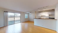 Located at 1560 Alice St in the heart of Oakland, CA, this single-floor residence offers a clean, modern layout designed for comfortable everyday living. The open-concept living and dining area is a standout feature, showcasing warm bamboo hardwood flooring, crisp white walls, and abundant natural light streaming through multiple windows and a full-width sliding glass door. The sliding door opens directly onto a private outdoor patio, providing a seamless indoor-outdoor connection. A ceiling fan adds to the comfort of the living space, while track lighting overhead ensures versatile illumination throughout.

The kitchen is thoughtfully designed in a galley style, featuring rich granite countertops, white cabinetry, track lighting, and tile flooring. It opens to the living area via a half-wall peninsula, maintaining an airy, connected feel. Additional rooms include a carpeted bedroom that receives generous natural light, lending a calm and restful atmosphere. The bathroom is neatly appointed with white tile surrounding a full soaking tub and shower combination, accented by a decorative mosaic tile border and complemented by granite countertops. Throughout the space, the consistent use of neutral tones and quality finishes creates a cohesive and inviting environment.
