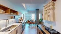 Located at 6390 De Longpre Ave in the heart of Hollywood, Los Angeles, this thoughtfully designed single-floor studio combines modern architecture with warm, organic aesthetics. The open-concept layout seamlessly connects the sleeping, living, and dining areas, creating a cohesive and functional living environment.

The galley-style kitchen is outfitted with light wood cabinetry featuring black hardware, a white quartz countertop, subway tile backsplash, stainless steel appliances including a full-size refrigerator and range, and built-in shelving — offering both style and practicality. A compact dining area with a round table and woven rattan chairs sits adjacent to large windows that invite ample natural light into the space.

A striking exposed cylindrical concrete column serves as a defining architectural element, anchoring the open layout and adding an industrial contrast to the warm wood tones and soft furnishings throughout. The sleeping area features light hardwood flooring, recessed lighting, and wall-mounted reading sconces.

The bathroom is clean and serene, finished with neutral tile, a wood vanity, built-in open shelving, and a walk-in shower. The entryway is framed by an arched full-length mirror and offers a clear sightline through the entire unit. Decorative art and natural textiles complete the warm, curated ambiance of this well-appointed Hollywood residence.