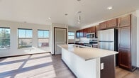 This single-floor residence showcases a thoughtfully designed open-concept layout with consistent, modern finishes throughout. The kitchen serves as a central hub, featuring rich dark-stained cabinetry that extends to the ceiling, stainless steel appliances including a refrigerator, range, and microwave, and a generously sized island with a light quartz countertop and an undermount sink. Pendant lighting above the island adds a contemporary touch, while hardwood-style flooring ties the kitchen seamlessly to the adjoining living areas.

Multiple rooms offer plush carpeting, ceiling fans, and abundant natural light through large windows that frame outdoor views of surrounding trees and neighboring structures. One bright room features a wall of windows on two sides, flooding the space with sunlight. A bedroom with private balcony access provides direct outdoor connectivity.

The bedrooms include closets with built-in shelving, and dark door and baseboard trim creates a striking contrast against the crisp white walls throughout. The bathroom is finished with wood-toned cabinetry, quartz countertops, a tub-shower combination, and wood-look vinyl flooring, completing the cohesive, modern aesthetic of this well-designed space.
