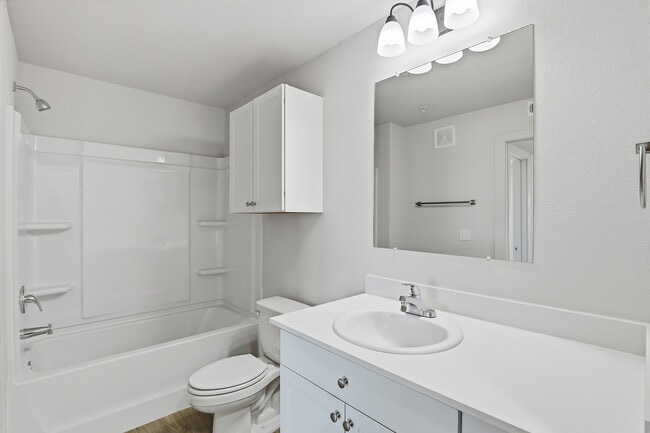 Pristine modern bathroom featuring sleek white cabinetry, elegant fixtures, and a spacious mirror, perfect for a contemporary living space. - Oaks at Mustang