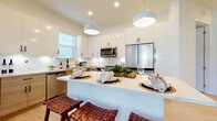Located at 19400 US Highway 19 N in Clearwater, Florida, this single-story residence showcases a clean, contemporary design with light wood-look flooring, white walls, and recessed lighting that create a bright, cohesive aesthetic throughout. The open-concept kitchen is a standout feature, outfitted with crisp white upper cabinetry, warm wood-toned lower cabinets, stainless steel appliances, and a white quartz countertop island with bar seating. Stylish pendant lights hang above the island, adding a modern touch to the well-appointed space. A hallway connects the kitchen to the living and sleeping areas, offering a smooth flow between rooms. The living area is generously proportioned, featuring multiple windows that allow abundant natural light and views of the surrounding greenery. Two bedrooms provide comfortable retreats, each with light flooring and access to closet space. Both bathrooms are finished with wood-grain vanities, white quartz countertops, subway tile surrounds, and tub-shower combinations. One bathroom offers direct access to a walk-in closet, adding practical functionality. The overall ambiance is calm, light-filled, and thoughtfully designed with a coastal-inspired aesthetic.