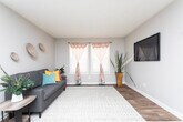 This single-floor residence offers a well-organized layout that balances communal living with private sleeping quarters. The open-plan living and dining area serves as the heart of the home, featuring warm wood-tone laminate flooring that adds depth and character to the space. A front entry door opens directly into this combined area, which comfortably accommodates both a seating arrangement and a dining set, making it ideal for everyday living and casual entertaining.

The galley-style kitchen runs along a dedicated corridor and is outfitted with white cabinetry extending to the upper walls, providing ample storage. Dark granite-style countertops contrast cleanly with the white surfaces, and the kitchen is equipped with a black electric range, a dishwasher, and a double sink — all the essentials for a fully functional cooking space.

The bedrooms are carpeted in a warm neutral tone, lending a cozy, comfortable feel. Each room is served by a sliding six-panel closet that maximizes floor space while offering practical storage. Ceiling fans support airflow throughout the sleeping areas. The overall interior palette is composed of soft gray and neutral tones, creating a calm and cohesive ambiance throughout the unit.