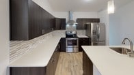 This single-floor home offers a well-designed layout across three bedrooms and two full bathrooms, providing ample living space throughout. The kitchen is a standout feature, showcasing dark espresso cabinetry with sleek hardware, crisp white quartz countertops, a mosaic tile backsplash, stainless steel appliances including a range with a wall-mounted hood vent and a French door refrigerator, and light wood-look flooring. A central island adds additional prep and counter space, complementing the kitchen's functional design.

The living area is notably spacious, featuring vaulted ceilings that enhance the sense of openness, plush carpeting, and a sliding glass door that leads to an outdoor balcony. Each bedroom is carpeted and equipped with a ceiling fan, with natural light provided by windows offering exterior views. One bedroom features an elegant arched window beneath a vaulted ceiling, adding architectural character.

The bathrooms include dark vanity cabinetry paired with stone-look countertops and light wood-look flooring. A dedicated laundry area houses a stacked washer and dryer unit alongside additional counter space, adding everyday convenience to this well-appointed home.