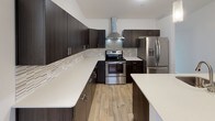This single-floor home offers a well-designed layout across three bedrooms and two full bathrooms, providing ample living space throughout. The kitchen is a standout feature, showcasing dark espresso cabinetry with sleek hardware, crisp white quartz countertops, a mosaic tile backsplash, stainless steel appliances including a range with a wall-mounted hood vent and a French door refrigerator, and light wood-look flooring. A central island adds additional prep and counter space, complementing the kitchen's functional design.

The living area is notably spacious, featuring vaulted ceilings that enhance the sense of openness, plush carpeting, and a sliding glass door that leads to an outdoor balcony. Each bedroom is carpeted and equipped with a ceiling fan, with natural light provided by windows offering exterior views. One bedroom features an elegant arched window beneath a vaulted ceiling, adding architectural character.

The bathrooms include dark vanity cabinetry paired with stone-look countertops and light wood-look flooring. A dedicated laundry area houses a stacked washer and dryer unit alongside additional counter space, adding everyday convenience to this well-appointed home.