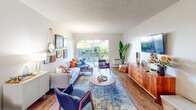 Located at 1151 Walnut Ave in Tustin, California, this single-story residence showcases a cohesive mid-century modern aesthetic throughout its thoughtfully designed layout. The open-concept living room serves as the heart of the home, featuring warm hardwood-style flooring, a curated gallery wall, and a large sliding glass door that invites abundant natural light while providing direct access to an outdoor area with lush greenery views. A warm-toned sectional sofa, mid-century accent chairs, and a richly colored area rug contribute to the inviting ambiance of this space. Adjacent to the living room, the dedicated dining area is highlighted by a ceiling fan with integrated lighting, hardwood-style flooring, and a bright window that keeps the space feeling airy and connected. The galley-style kitchen is efficiently designed with contemporary dark cabinetry, light countertops, and stainless steel appliances, including a refrigerator, range, and built-in microwave. The bedroom offers plush carpeting, a generously sized walk-in closet, and a sliding glass door that frames outdoor views. The bathroom is clean and modern, featuring wood-style flooring, a combination tub and shower, and a sleek vanity with ample storage. Throughout the home, neutral tones, textured ceilings, and stylish finishes create a warm and livable atmosphere.