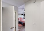 Located at 6350 Griffin Rd in Davie, Florida, this single-floor studio unit offers a thoughtfully designed, all-in-one living space ideal for students or solo residents. The main living area centers around a built-in bed frame integrated with a floor-to-ceiling shelving and storage unit, providing ample space for books, décor, and personal items alongside a dedicated desk and chair — making it well-suited for studying and everyday living. Light wood-style flooring runs throughout, complementing the clean white walls and giving the space a bright, modern feel. A ceiling fan overhead provides air circulation, and a window with blinds allows for natural light. The kitchenette is efficiently laid out with dark espresso cabinetry, granite-style countertops, a stainless steel refrigerator, built-in microwave, sink, and dishwasher — offering full meal preparation capability within a compact footprint. The private bathroom features neutral tile flooring, a dark-toned vanity with granite countertop and single sink, a large mirror with overhead lighting, and a standout frameless glass corner shower enclosure. The overall design of this unit balances functionality and comfort, making efficient use of every square foot while maintaining a clean, contemporary aesthetic throughout.