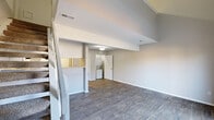 Located at 6317 Shanda Dr in Raleigh, NC, this two-floor home is thoughtfully designed to maximize its compact footprint across two distinct levels. The main floor forms the heart of the home, featuring an open living area with durable wood-style flooring, neutral gray walls, and soaring ceilings that enhance the sense of space. A sliding glass door allows natural light to pour in and provides direct access to an outdoor deck with views of the surrounding landscape. The kitchen is well-appointed with stainless steel appliances, including a range and refrigerator, white cabinetry, and light wood-style flooring, lending a clean and modern aesthetic. A dedicated laundry area is conveniently tucked within the main level. Upstairs, the loft-style second floor offers a cozy retreat with plush carpeting, a ceiling fan, and a well-organized walk-in closet outfitted with built-in shelving, providing ample storage solutions. The bathroom completes the layout, contributing to the home's functional design. Throughout the space, a consistent neutral color palette and clean finishes create a bright, cohesive ambiance. The staircase connecting the two levels adds architectural interest while maintaining an efficient use of the overall floor plan.