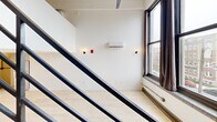 Located at 220 S 47th St in West Philadelphia, this three-floor unit offers a distinctive multi-level layout with a modern industrial aesthetic throughout. The space is distributed across three floors, with the main living level serving as the largest and most functional area, featuring light hardwood flooring, crisp white walls, and oversized windows that frame neighborhood views and draw in natural light. A sleek, dark steel open-riser staircase serves as a striking architectural centerpiece, connecting the floors while adding a bold visual contrast to the bright interior. The kitchen is equipped with stainless steel appliances, dark wood cabinetry, and a clean countertop workspace positioned adjacent to the staircase. A wall-mounted mini-split HVAC unit ensures climate control throughout. The upper level provides an additional open area illuminated by track lighting with exposed industrial ceiling details, ideal for flexible use. The bathroom features a fully tiled walk-in shower with large-format white tiles, chrome fixtures, and a clean, modern vanity. Two hallways facilitate circulation between levels. With four staircases connecting this compact vertical layout, the unit offers a dynamic and efficiently organized living environment.