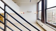 Located at 220 S 47th St in West Philadelphia, this three-floor unit offers a distinctive multi-level layout with a modern industrial aesthetic throughout. The space is distributed across three floors, with the main living level serving as the largest and most functional area, featuring light hardwood flooring, crisp white walls, and oversized windows that frame neighborhood views and draw in natural light. A sleek, dark steel open-riser staircase serves as a striking architectural centerpiece, connecting the floors while adding a bold visual contrast to the bright interior. The kitchen is equipped with stainless steel appliances, dark wood cabinetry, and a clean countertop workspace positioned adjacent to the staircase. A wall-mounted mini-split HVAC unit ensures climate control throughout. The upper level provides an additional open area illuminated by track lighting with exposed industrial ceiling details, ideal for flexible use. The bathroom features a fully tiled walk-in shower with large-format white tiles, chrome fixtures, and a clean, modern vanity. Two hallways facilitate circulation between levels. With four staircases connecting this compact vertical layout, the unit offers a dynamic and efficiently organized living environment.