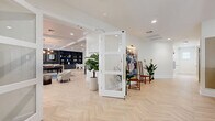 Located at 5201 W Hillsboro Blvd in Coconut Creek, Florida, this thoughtfully designed community amenity space offers a generous single-floor layout brimming with upscale social and recreational features. Throughout, light-toned herringbone hardwood flooring establishes a refined aesthetic, complemented by crisp white walls, coffered and tray ceilings with recessed lighting, and an abundance of natural light through large windows.

The main lounge is anchored by a large-screen TV and a plush seating arrangement featuring a bold orange sectional sofa, a sleek billiards table, and a built-in wet bar with counter seating. Adjacent areas include a dining nook with deep navy velvet booth seating set against a lush tropical mural, a navy-accented shelving wall, and cozy lounge seating throughout.

A dedicated entertainment wing houses an HD Golf simulator with projector and bar seating, a foosball table, a Golden Tee PGA Tour arcade console, and a putting green surface — making it a standout recreational hub. The entry corridor welcomes visitors with curated artwork, decorative plants, and refined furnishings. Glass-paneled French doors and open sightlines connect the spaces fluidly, giving the entire floor a seamless, social atmosphere ideal for community gatherings.