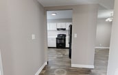 This two-story residence at 500 Piccadilly Row in Antioch, TN offers 1,590 square feet of living space across two well-appointed floors. The main floor (780 sq ft) features an open living room with striking high ceilings, a white brick fireplace, and durable wood-look plank flooring that extends throughout the common areas. Natural light filters in through window blinds, enhancing the neutral warm-gray color palette. The kitchen is equipped with white cabinetry, white countertops, a built-in dishwasher, and a window above the sink. A combined dining and living area with a modern multi-bulb ceiling fixture provides additional flexible space. The upper floor (810 sq ft) houses all four bedrooms, each featuring plush carpeting, closets with sliding or hinged doors, and windows with outdoor views. The primary bedroom measures 180 square feet. Three bathrooms serve the home: two include a tub/shower combo or walk-in shower with white tile surround, white vanities, and wood-look flooring. A dedicated laundry closet with a full-size washer and dryer adds everyday convenience. A carpeted staircase connects both floors, completing this functional and well-designed home.