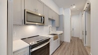Located at 10400 Research Blvd in Austin, TX, this single-floor, one-bedroom, one-bathroom unit offers a well-designed layout with modern finishes throughout. The kitchen is a standout feature, showcasing gray shaker-style cabinetry extending to the ceiling, a white hexagonal tile backsplash, quartz countertops, a stainless steel farmhouse sink, and a full suite of stainless steel appliances including a refrigerator, range, microwave, and dishwasher. Light wood-style flooring runs through the main living and kitchen areas, creating a clean and cohesive look. The bedroom is carpeted for comfort, features neutral white walls, and is equipped with a ceiling fan. It offers a cozy, functional space suitable for a variety of furniture arrangements. The bathroom is thoughtfully appointed with gray shaker vanity cabinetry, a white quartz countertop, a well-lit mirror, light tile flooring, and a glass-enclosed walk-in shower. The overall aesthetic throughout the unit is contemporary and neutral, with consistent use of gray and white tones, clean lines, and quality finishes that contribute to a polished, move-in-ready atmosphere.