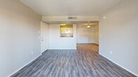 Located at 6570 W Flamingo Rd in Las Vegas, NV, this one-bedroom, one-bathroom apartment offers a well-organized, single-floor layout designed for comfortable everyday living. The open-concept living room and kitchen area features wood-style laminate flooring that runs throughout the main living spaces, neutral gray walls, and a textured ceiling. A pass-through window connects the living area to the kitchen, while a sliding glass door leads out to a private balcony with views of the surrounding palm tree-lined exterior. The galley-style kitchen is efficiently arranged with white cabinetry, dark countertops, a gas range, built-in microwave, refrigerator, and a dedicated pantry closet — all illuminated by an overhead flush-mount light fixture. The bedroom is carpeted for comfort, features a ceiling fan with light, and receives natural light through a window with exterior views. The full bathroom includes a tub-shower combination with white tile surround, wood-style flooring, a vanity with a stone-look countertop, and a well-lit mirror. A dedicated laundry area houses a full-size side-by-side washer and dryer, adding significant convenience to the unit.