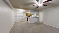 This single-floor, 2-bedroom, 1-bathroom residence offers a practical and functional layout designed to maximize its comfortable footprint. The open-concept main living area combines the living room, dining space, and kitchen into one cohesive zone, creating a welcoming and versatile environment. A standout feature of the living room is the white-painted wood-burning fireplace with decorative panel detailing and built-in display shelving flanking the adjacent wall — ideal for storage and display. A ceiling fan overhead and plush carpeting underfoot add to the room's comfort. The galley-style kitchen is well-equipped with warm-toned wood cabinetry lining both walls, light speckled countertops, a white appliance suite including a range and refrigerator, and a single-basin sink. A skylight fixture brightens the kitchen, while light hardwood-style flooring provides a clean, durable surface. A peninsula counter offers a casual dining or prep area. Both bedrooms are carpeted and feature ceiling fans with lighting. The primary bedroom is generously proportioned and includes access to the bathroom. The unit also includes two closets and a dedicated laundry area. A textured ceiling is consistent throughout, and sliding glass doors in the living area provide natural light and outdoor access.