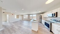 This 1-bedroom, 1-bathroom unit in Manchester, New Hampshire offers a thoughtfully designed open-concept layout that seamlessly connects the kitchen and living areas. Light-toned luxury vinyl plank flooring flows throughout the space, enhancing the bright and airy atmosphere created by recessed lighting and large, multi-pane windows that frame views of the surrounding cityscape.

The kitchen is a standout feature, equipped with white shaker-style cabinetry, granite countertops, and a full suite of stainless steel appliances including a refrigerator, electric range, and over-the-range microwave. A central island with a built-in sink adds both functionality and a natural gathering point, anchoring the open living space.

The generously sized living area benefits from abundant natural light pouring in through oversized windows, offering elevated views of downtown Manchester. The open floor plan allows for flexible furniture arrangements and a sense of spaciousness throughout.

The bathroom is clean and well-appointed, featuring a white vanity with granite countertop, a framed mirror, and consistent finishes that complement the rest of the unit. Additional doors visible in the layout suggest ample closet and storage space. The overall design is modern, neutral, and move-in ready.
