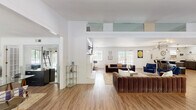 Located at 301 W Vandalia Rd in Greensboro, NC, this single-floor space offers a well-appointed and multifunctional layout designed to accommodate a variety of uses. The interior is anchored by a spacious open living area finished with warm wood-tone luxury vinyl plank flooring that runs throughout, crisp white walls, and elevated ceilings accented by an upper-level glass panel feature that adds architectural interest and visual depth.

The main living area is generously sized, accommodating multiple seating arrangements including plush velvet sofas and accent chairs, centered around a coffee table and complemented by curated wall art. Natural light pours in through multiple windows and a set of French doors, creating a bright and welcoming atmosphere.

An adjacent office zone features glass-top desks, a lean ladder bookshelf, and ample natural light from surrounding windows with classic wood wainscoting detail, making it a productive and stylish workspace.

The recreation area is highlighted by a bold dark wood plank accent wall, a pool table, and open floor space, flowing seamlessly into a kitchenette outfitted with counter seating, pendant lighting, dark cabinetry, a microwave, and a mini-refrigerator — ideal for hosting or daily use. The overall ambiance is modern, functional, and inviting.