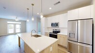 This thoughtfully designed 2-bedroom, 3-bathroom residence at 2418 Main St in Rocky Hill, Connecticut offers a clean, modern aesthetic throughout its single-floor layout. The open-concept kitchen serves as the heart of the home, featuring a large waterfall-edge island with an undermount sink, crisp white upper cabinetry paired with warm natural wood lower cabinets, stainless steel appliances including a French door refrigerator, electric range, and built-in microwave, all illuminated by a trio of elegant glass pendant lights. Light hardwood-style flooring flows seamlessly through the kitchen and living areas, complementing the neutral color palette. The spacious living area is bathed in natural light through French doors that open to a balcony, with a ceiling fan adding comfort overhead. Both bedrooms are carpeted for warmth and each is equipped with a ceiling fan and window with exterior views. The generously sized primary bedroom includes an en-suite bathroom with a wood-toned vanity, white quartz countertop, stylish gold sconce lighting, and access to a walk-in closet with wire shelving systems. Two additional closets provide ample storage throughout. Clean white panel doors with matte black hardware add a refined, contemporary touch to every room.