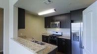 This two-story residence offers a thoughtfully designed layout spread across two levels, providing ample space for comfortable everyday living. The kitchen stands out as a focal point of the home, showcasing rich dark cabinetry that contrasts elegantly with light granite countertops featuring subtle veining and warm tones. Stainless steel appliances, including a gas range, built-in microwave, and refrigerator, lend the kitchen a sleek, contemporary aesthetic. A peninsula with a double basin sink extends from the main counter, creating a practical workspace while also serving as a natural divider between the kitchen and adjoining living areas. Recessed and overhead lighting ensures the kitchen remains bright and functional. The neutral wall tones complement the dark cabinetry, contributing to a cohesive and modern interior palette. The two-floor configuration of the residence allows for a natural separation between living and private spaces, enhancing both functionality and privacy. Overall, the space presents a clean, modern design sensibility with durable, high-quality finishes that balance style with practicality.