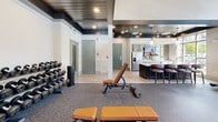 Located at the Enclave Piney community in Asheville, NC, this fitness center is a thoughtfully designed amenity space that seamlessly blends function with upscale aesthetic. The single-floor layout offers a generous open floor plan with dedicated zones for cardio and strength training, all unified by durable speckled rubber flooring suited for high-performance workouts.

A dramatic floor-to-ceiling stone fireplace serves as the room's architectural centerpiece, topped with a mounted flat-screen TV and a rustic wood mantel that adds warmth and character. Adjacent to the fireplace, a rack of kettlebells, medicine balls, and exercise accessories provides convenient access to supplemental fitness tools.

The strength training area is outfitted with cable machines, a multi-functional weight station, adjustable benches, and a full dumbbell rack, catering to a wide range of workout routines. The cardio zone features treadmills, ellipticals, and a stair climber, positioned beneath soaring two-story windows that flood the space with natural light and offer views of the surrounding landscape.

Overhead, a striking dark wood-paneled ceiling with recessed lighting adds a sophisticated contrast to the bright, airy walls. French doors open directly to the outdoor pool area, enhancing the sense of openness. A small kitchenette with bar seating is also present, rounding out this comprehensive and stylish community fitness facility.