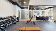 Located at the Enclave Piney community in Asheville, NC, this fitness center is a thoughtfully designed amenity space that seamlessly blends function with upscale aesthetic. The single-floor layout offers a generous open floor plan with dedicated zones for cardio and strength training, all unified by durable speckled rubber flooring suited for high-performance workouts.

A dramatic floor-to-ceiling stone fireplace serves as the room's architectural centerpiece, topped with a mounted flat-screen TV and a rustic wood mantel that adds warmth and character. Adjacent to the fireplace, a rack of kettlebells, medicine balls, and exercise accessories provides convenient access to supplemental fitness tools.

The strength training area is outfitted with cable machines, a multi-functional weight station, adjustable benches, and a full dumbbell rack, catering to a wide range of workout routines. The cardio zone features treadmills, ellipticals, and a stair climber, positioned beneath soaring two-story windows that flood the space with natural light and offer views of the surrounding landscape.

Overhead, a striking dark wood-paneled ceiling with recessed lighting adds a sophisticated contrast to the bright, airy walls. French doors open directly to the outdoor pool area, enhancing the sense of openness. A small kitchenette with bar seating is also present, rounding out this comprehensive and stylish community fitness facility.