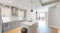 This thoughtfully designed 2-bedroom, 1-bathroom residence at 350 Carraway Crossing in Chapel Hill, NC offers a modern, open-concept layout with clean lines and contemporary finishes throughout. The kitchen serves as a central showpiece, featuring two-tone shaker cabinetry in white and soft gray with matte black hardware, quartz countertops, a central island with an undermount sink, stainless steel appliances including a wall oven and built-in microwave, and a dedicated wine rack. Pendant lighting adds a stylish accent above the island. The kitchen flows seamlessly into the living area, where light wood-style flooring and neutral warm-toned walls create a bright, welcoming ambiance. Large floor-to-ceiling windows in the primary bedroom flood the space with natural light while offering expansive views of the Chapel Hill skyline and surrounding greenery. The bathroom is elegantly appointed with a dual-sink vanity, dark countertops, white shaker cabinetry, and large-format tile flooring. A generously sized walk-in closet with built-in shelving and hanging rods provides ample storage. Additional conveniences include an in-unit laundry room with a full-size washer and dryer, a dedicated hallway, and an extra closet for additional storage needs.