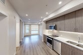 Located at 5112 Elbow Dr SW in Calgary, Alberta, this thoughtfully designed one-bedroom, one-bathroom unit offers a contemporary living experience across a single floor. The open-concept layout connects the kitchen and living area seamlessly, creating an efficient and functional flow throughout the space. Recessed lighting illuminates the interior, complemented by light wood-tone laminate flooring that runs consistently through all main areas.

The kitchen is a standout feature, outfitted with a full suite of stainless steel appliances including a slide-in range, built-in microwave, dishwasher, and refrigerator. Rich, wood-grain cabinetry extends to the ceiling, providing generous storage, while a white quartz countertop and a neutral tile backsplash complete the modern aesthetic. The living area receives natural light through large double doors and windows facing the exterior.

The bedroom is a quiet retreat featuring oversized windows with views of the surrounding neighbourhood and ample closet space. The four-piece bathroom is finished with warm wood cabinetry, a white quartz vanity, large format floor tiles, and a full soaker tub with shower. A dedicated in-suite laundry area houses a stacked washer and dryer unit, adding everyday convenience to this well-appointed home.