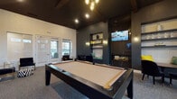 Located at 12000 West Fairview Avenue in Boise, Idaho, this sophisticated single-floor amenity lounge is designed to impress. The space is anchored by a dramatic vaulted ceiling with exposed wood beams, creating a sense of grandeur and openness throughout. A striking modern chandelier with globe-style pendants serves as a central focal point, complementing the recessed lighting that illuminates the room.

The game room area is centered around a sleek, dark-framed pool table with a neutral felt surface, while a shuffleboard table provides additional entertainment options. Deep charcoal accent walls contrast beautifully with lighter wall textures, lending the space a bold yet refined atmosphere. Built-in shelving niches display decorative accents and flank a contemporary fireplace with a glass front, adding warmth and visual interest. A built-in window seat with teal cushions offers a cozy nook, and multiple mounted flat-screen televisions ensure entertainment throughout.

The lounge area includes intimate seating arrangements with dark velvet chairs and small bistro tables, ideal for socializing. Adjacent to the game room, the reception and entry area features textured light-toned walls, large windows that invite natural light, and stylish navy velvet armchairs with gold-frame accents, creating a welcoming and upscale first impression. Carpeted flooring in a neutral tone ties the entire space together cohesively.